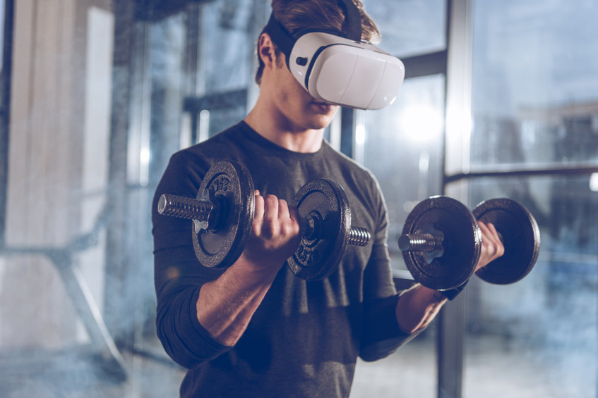 Mann testet einen Fitness Trend mit Hanteln und Virtual Reality Headset