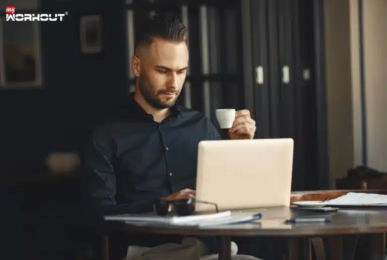 Die Wirkung von Koffein – So funktioniert der Wachmacher Mann sitzt am Tisch an seinem Laptop und nimmt Koffein in Form von Espresso zu sich